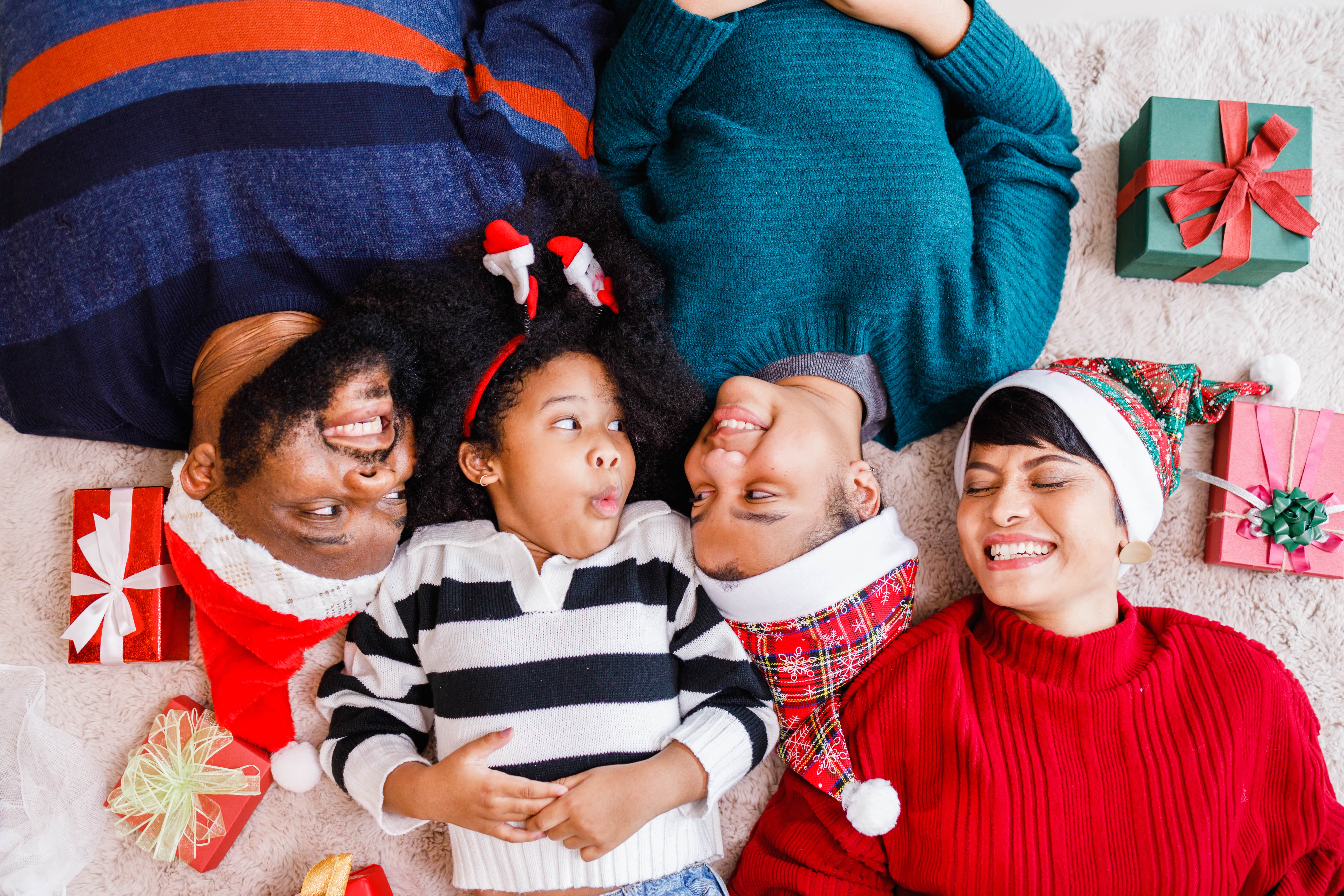 A young family laying on the floor in Holiday outfits laughing together.